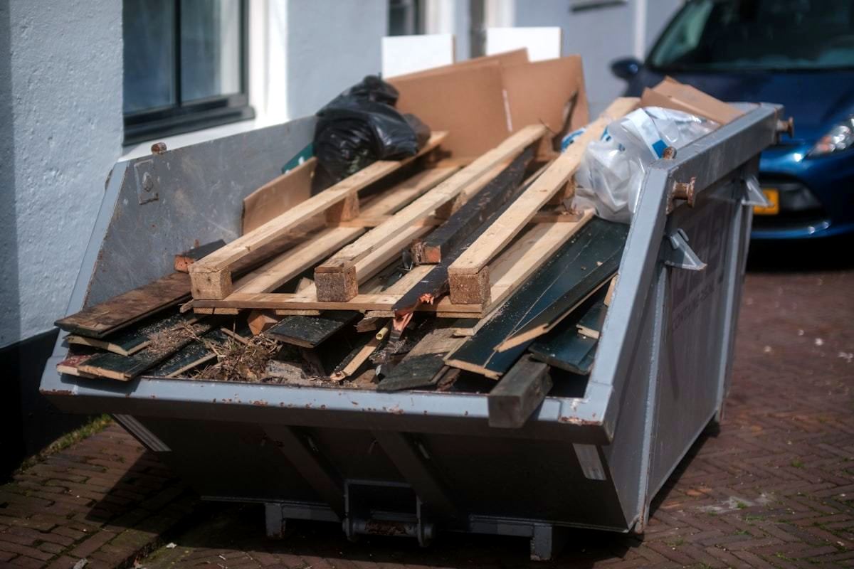 A skip loaded with timber, floorboards and renovation offcuts outside a house.